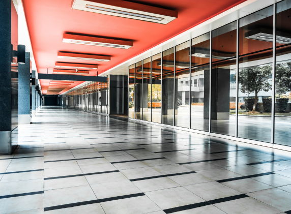 A modern commercial building interior with a long corridor, large glass windows, red ceiling, and geometric tile flooring
