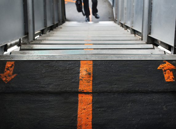 A set of metal stairs with an orange line running down the center and arrows pointing in opposite directions at the bottom