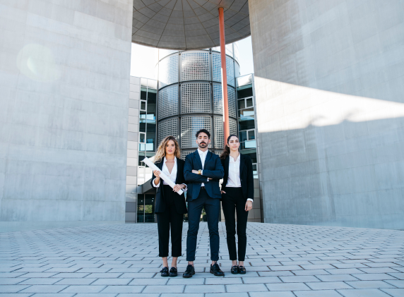Three professionals standing in front of a modern building, holding architectural plans
